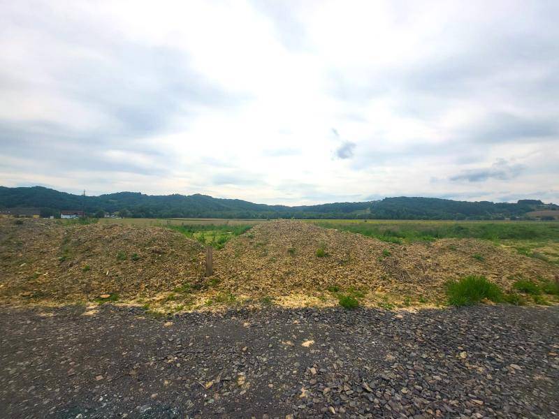 Schotterweg führt zu Erdhügeln mit weitem Blick auf die umliegende Landschaft und Hügel.