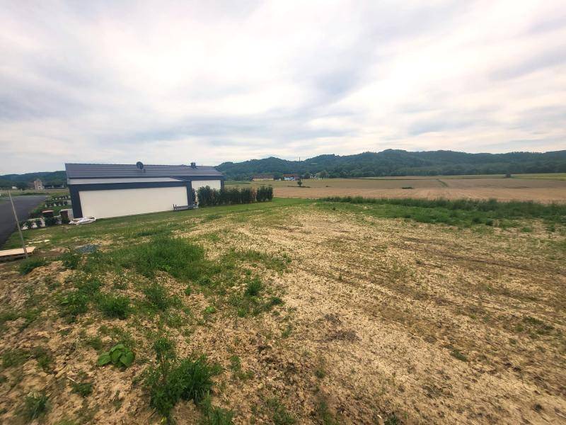 Undeveloptes Grundstück mit einem modernen Haus im Hintergrund und weitem Blick auf die Landschaft.