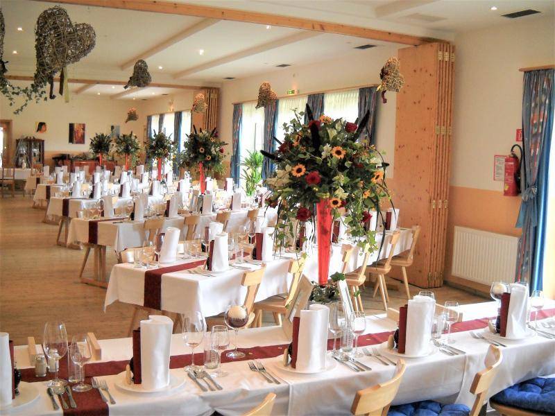 Großer Speisesaal festlich dekoriert mit langen Tischen, weißen Tischdecken und Blumenarrangements.