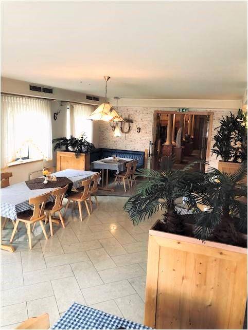 Heller Essbereich mit karierten Tischdecken, Holztischen und Pflanzen in Holzkübeln.