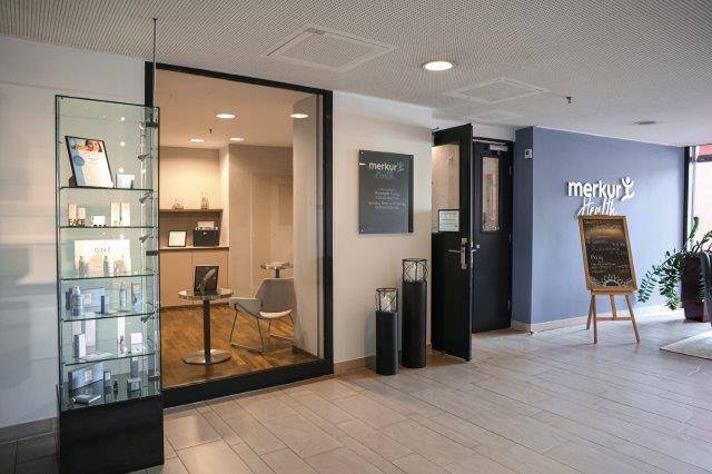Eingangsbereich zu einer Gesundheitseinrichtung mit Glasvitrine und Fliesenboden.
