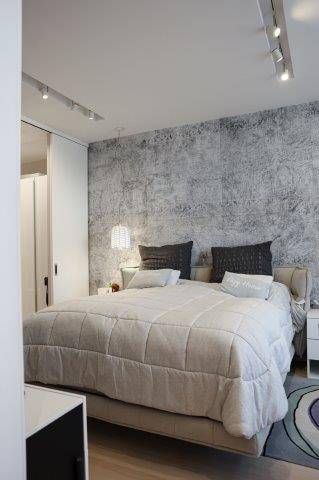 Helles Schlafzimmer mit Doppelbett, strukturierter Wand und modernem Beleuchtungssystem, sehr gemütlich.