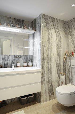 Modernes Badezimmer mit Marmoroptik-Fliesen, Waschtisch und wandhängendem WC, elegant und funktional.