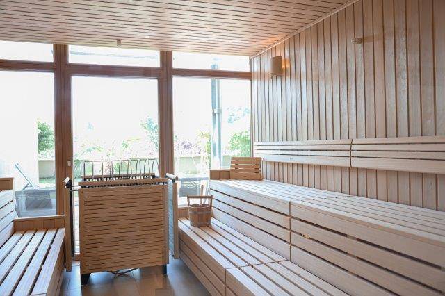 Helle Sauna mit Holzverkleidung, mehrstufigen Bänken und großen Fenstern.