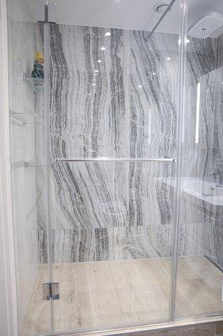 Moderne Duschkabine mit Glaswänden und Marmoroptik-Fliesen im Badezimmer, bietet viel Komfort.