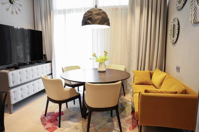Gemütlicher Essbereich mit rundem Holztisch, gelbem Sofa und modernem Teppich, lädt zum Verweilen ein.