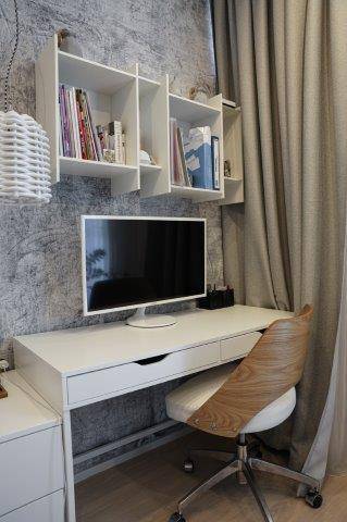 Moderner Arbeitsplatz mit weißem Schreibtisch, Monitor und Regalen an der Wand, gut organisiert.