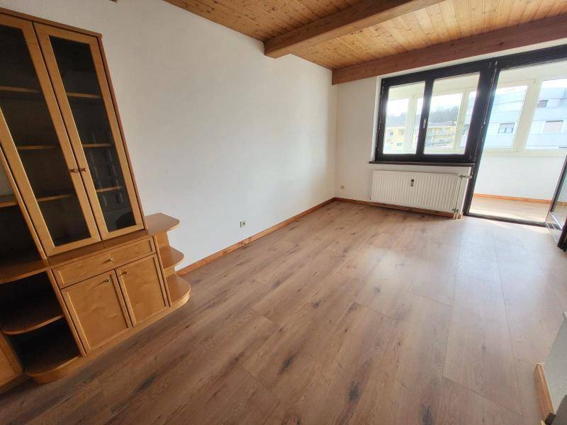 Wohnzimmer mit Holzdecke, Laminatboden und Zugang zu einem verglasten Balkonbereich.