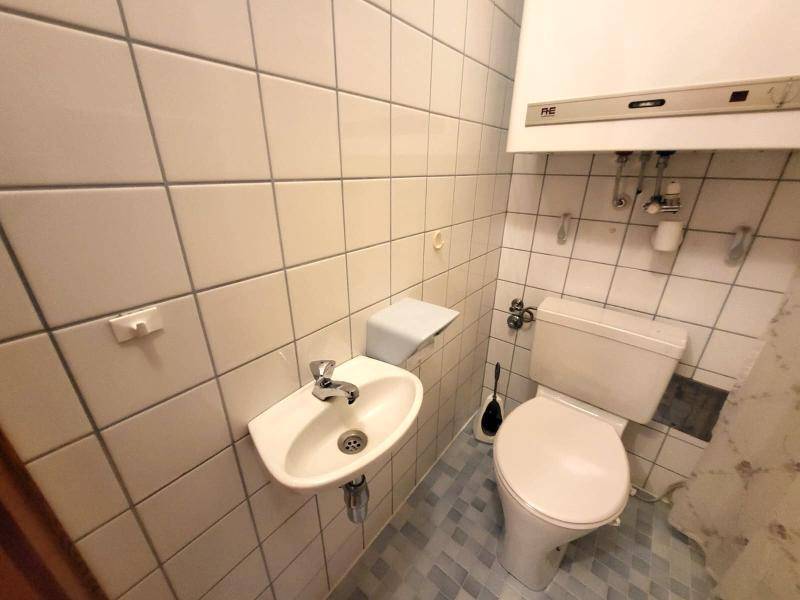 Kleines Gäste-WC mit Toilette, Waschbecken und hellen Wandfliesen.