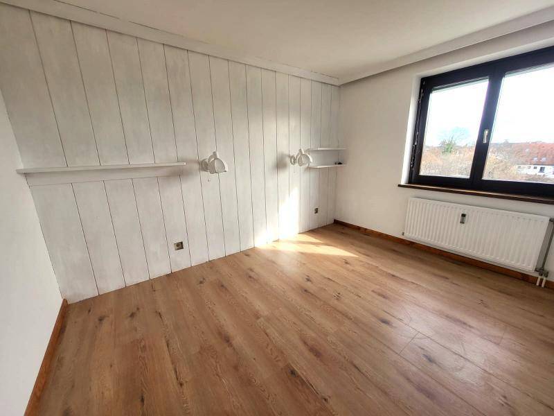 Zimmer mit Laminatboden, weißer Holzpaneelwand und Fenster für natürliches Licht.