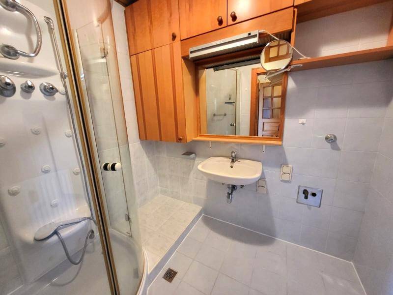 Badezimmer mit Duschkabine, Waschbecken und Spiegelschrank, hell gefliest.
