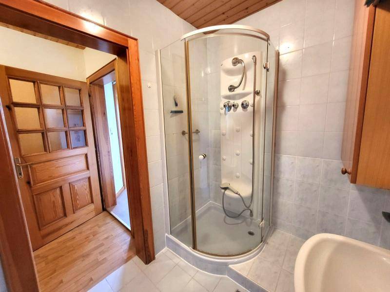 Badezimmer mit Duschkabine, hellen Fliesen und Holzdecke, funktional eingerichtet.