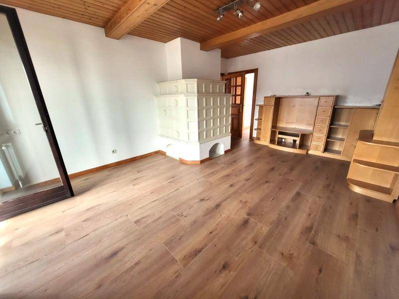 Gemütliches Wohnzimmer mit traditionellem Kachelofen, Holzbalkendecke und Laminatboden.