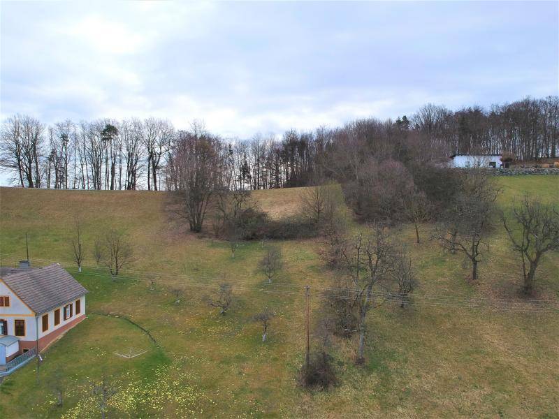 Luftaufnahme des Grundstücks mit einem Haus, weiten Wiesenflächen und einem bewaldeten Hügel im Hintergrund.
