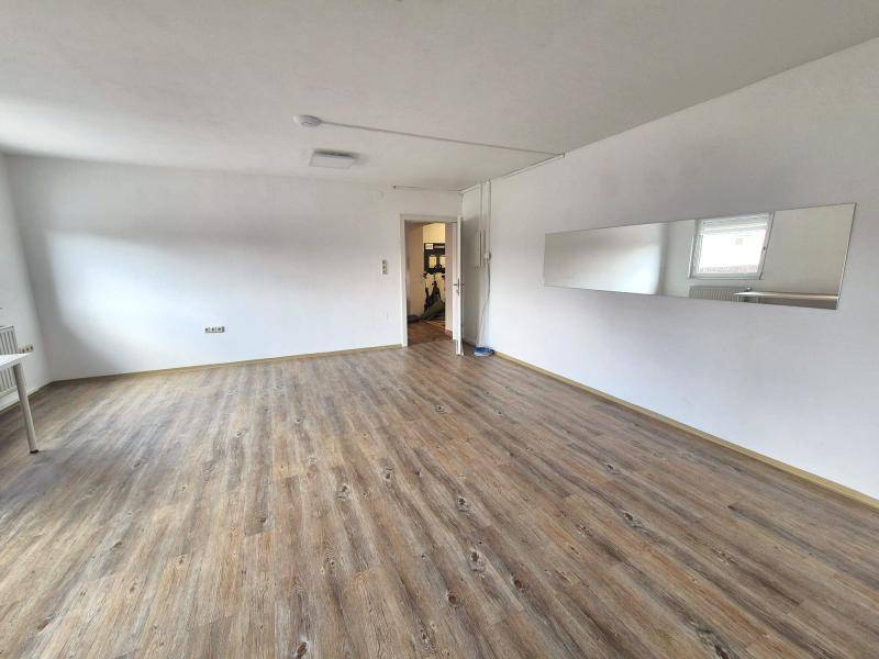 Blick in den geräumigen Wohnbereich mit Laminatboden, weiß gestrichenen Wänden und einem Wandspiegel.