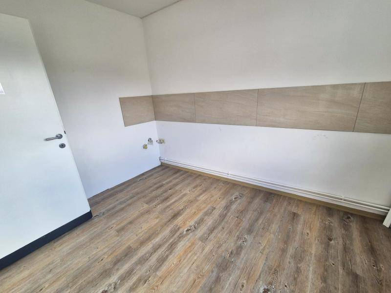 Blick in einen Raum mit Laminatboden, weiß gestrichenen Wänden und einer Fliesenverkleidung im unteren Bereich.