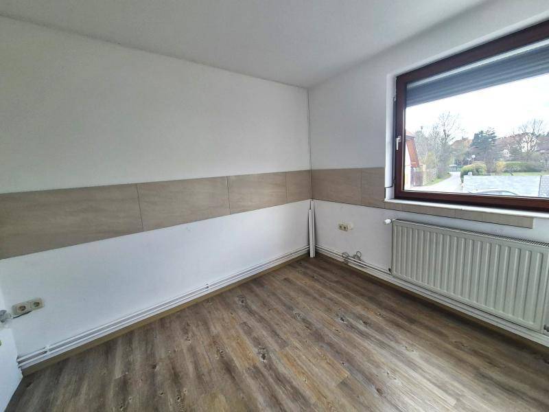Raum mit Laminatboden, weißen Wänden und einer horizontalen Fliesenband, Blick aus dem Fenster ins Grüne.