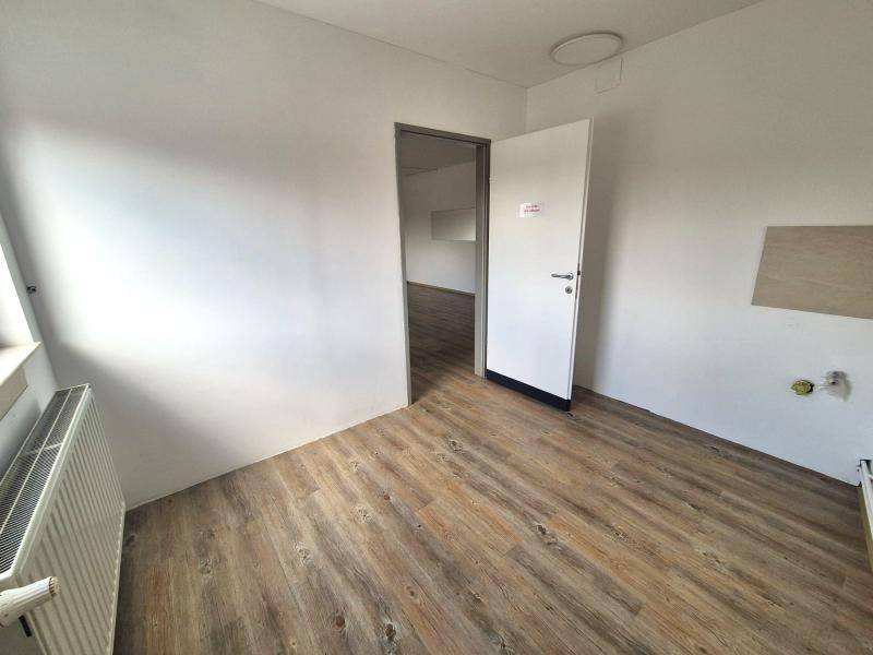 Heller Raum mit Laminatboden und weißer Wandfarbe, ein offener Durchgang führt in einen weiteren Bereich.
