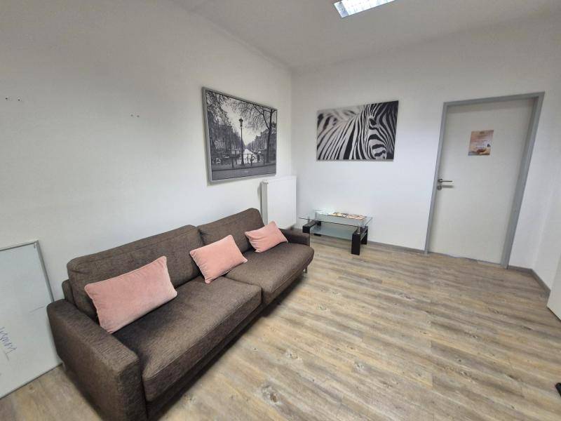 Heller Wartebereich mit beigem Sofa, Couchtisch und modernen Kunstwerken an den Wänden.