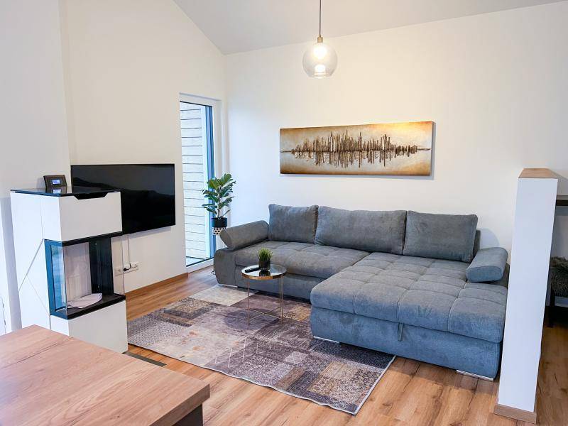 Helles Wohnzimmer mit großem Ecksofa, modernem Kamin und Holzboden, lädt zum Entspannen ein.