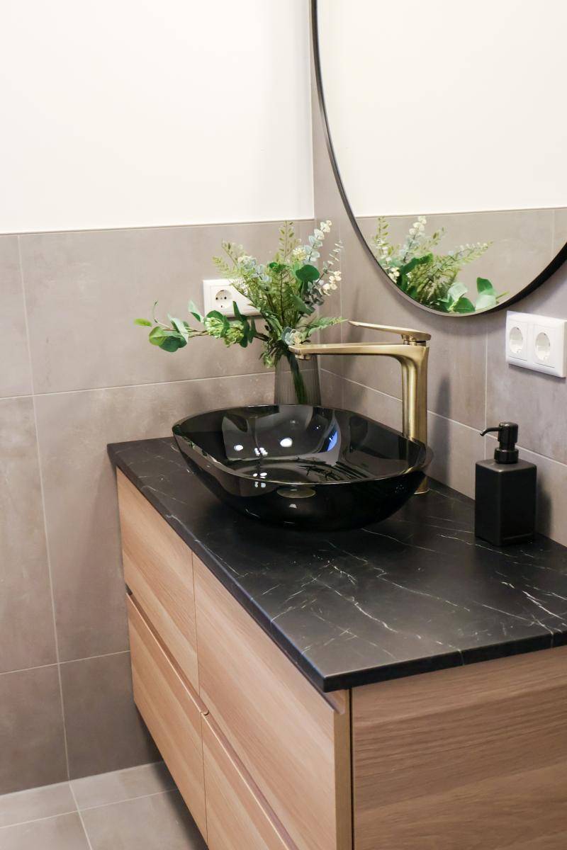 Detailansicht des modernen Waschtischs mit schwarzem Aufsatzbecken und goldenem Wasserhahn.