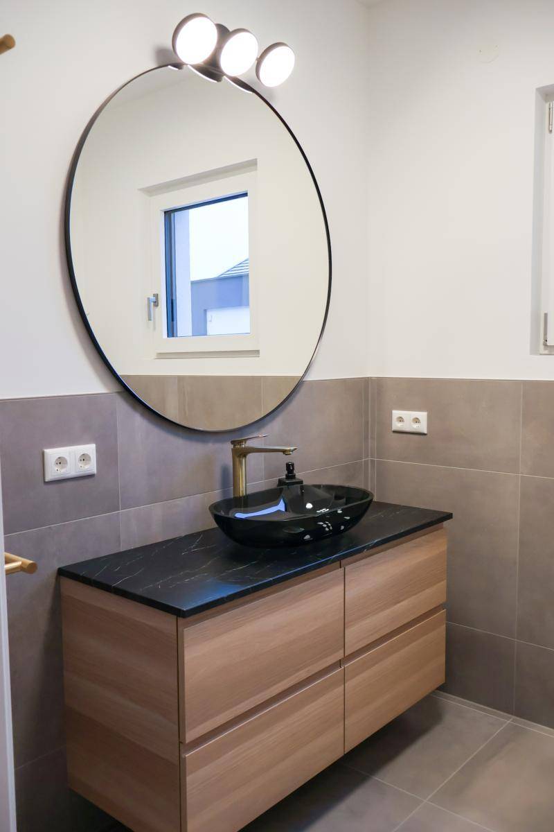Modernes Badezimmer mit Holzwaschtisch, schwarzem Aufsatzwaschbecken und großem Rundspiegel.