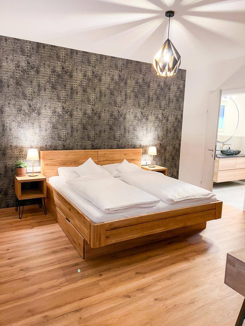 Gemütliches Schlafzimmer mit Holzbett, Nachttischen und auffälliger Tapete, bietet eine warme Atmosphäre.
