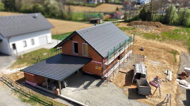 Neubau im Rohbau mit integriertem Carport und umliegendem Baugrundstück.
