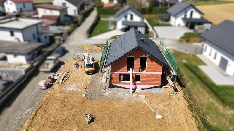 Draufsicht auf ein im Bau befindliches Haus mit Dachziegeln und offener Baugrube.