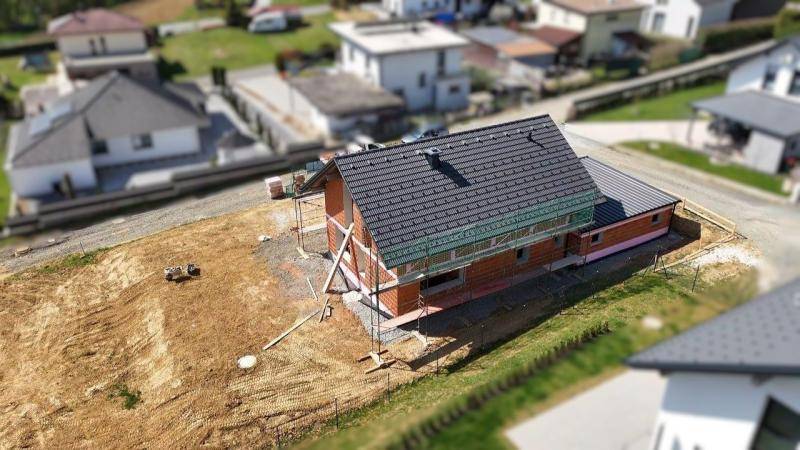 Luftaufnahme eines Neubaus mit bereits gedecktem Dach und vorbereiteter Fassade.