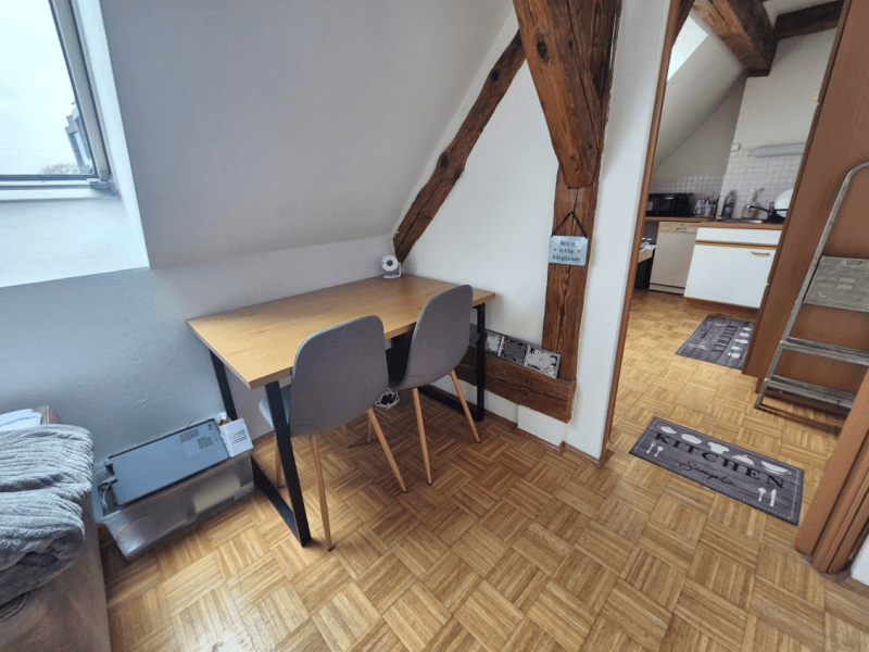 Kleiner Essbereich oder Arbeitsplatz im Dachgeschoss mit Holzbalken und Parkettboden, ideal für zwei Personen.