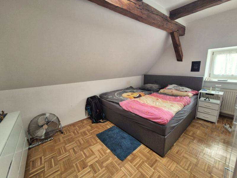 Schlafzimmer im Dachgeschoss mit Doppelbett, Parkettboden und sichtbaren Holzbalken, bietet eine gemütliche Atmosphäre.