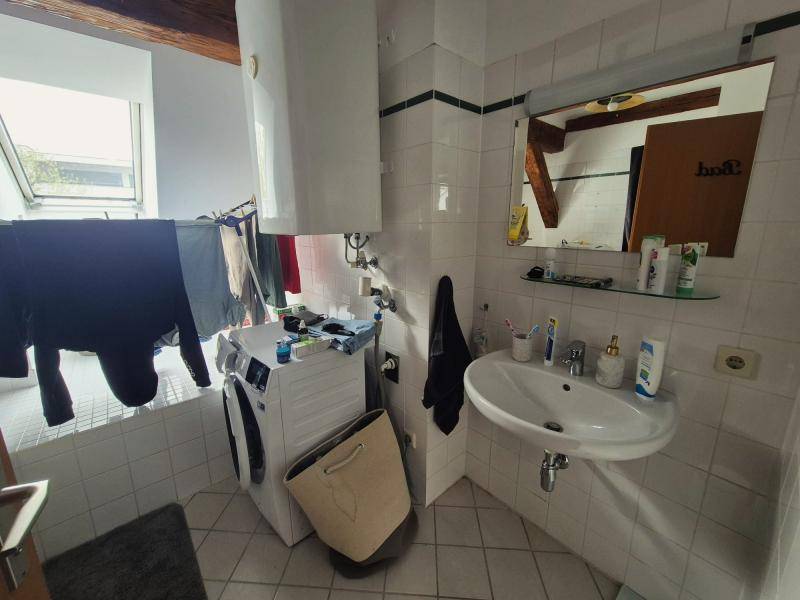 Badezimmer mit Waschbecken, Spiegel und Waschmaschine unter einem Dachfenster, praktisch und hell.