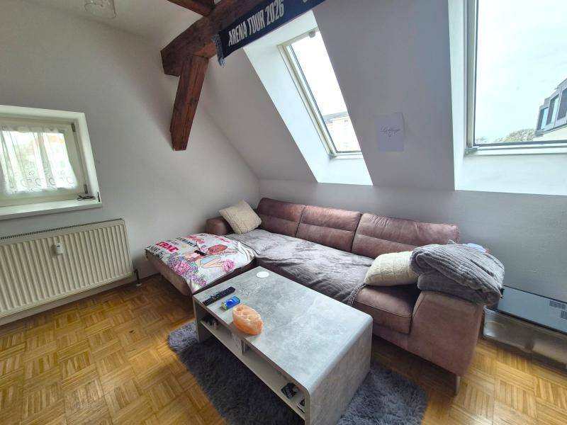 Gemütlicher Wohnbereich mit brauner Couch, Dachfenstern und Holzbalken im Dachgeschoss, hell und einladend.