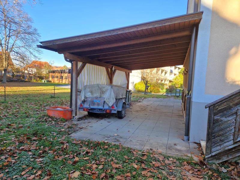 Überdachter Carport-Bereich mit gepflastertem Boden und einem Anhänger.