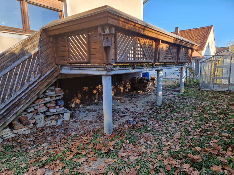 Erhöhter Holzbalkon mit Geländer und Blick auf den Gartenbereich mit Herbstlaub.