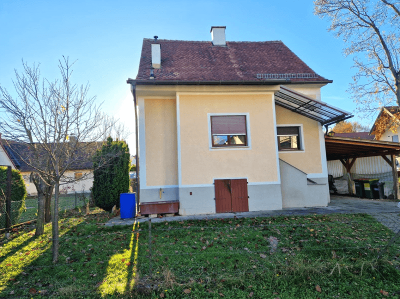Seitenansicht des Hauses mit Gartenbereich, einem Carport und einem Fenster mit Rollladen.