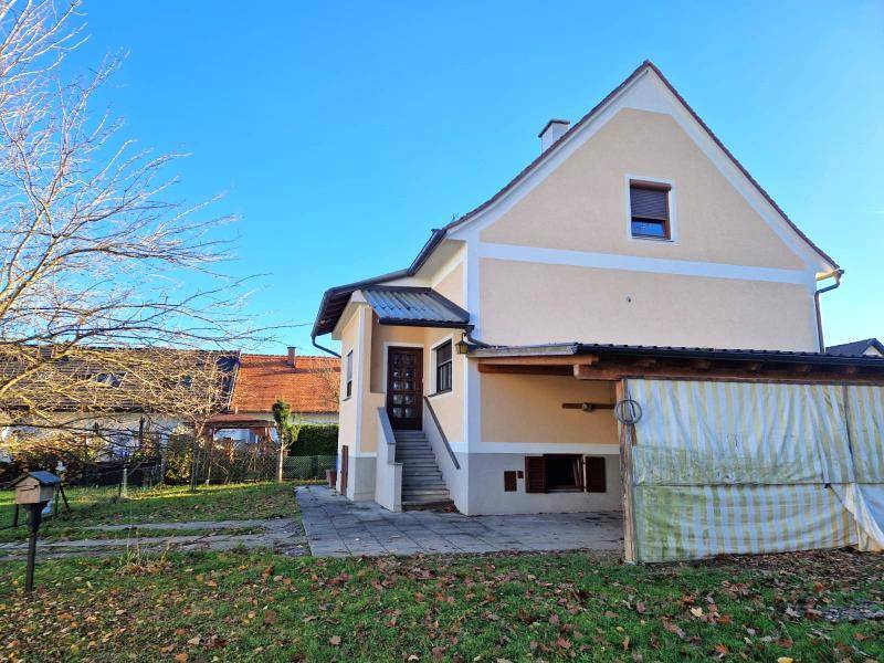 Ansicht des Hauses mit Eingangsbereich, Treppe und einem überdachten Unterstand.