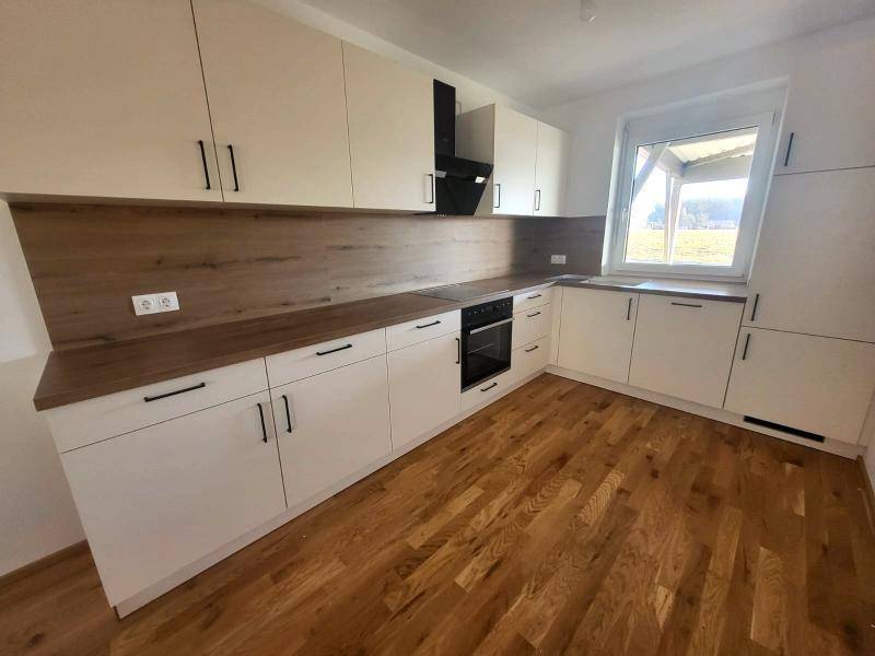 Moderne Einbauküche mit weißen Schränken, Holzarbeitsplatte und Holzboden.