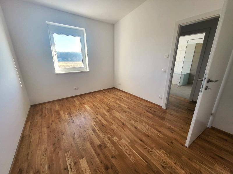 Helles Schlafzimmer mit Holzboden und Fenster, das einen weiten Blick auf die Natur bietet.