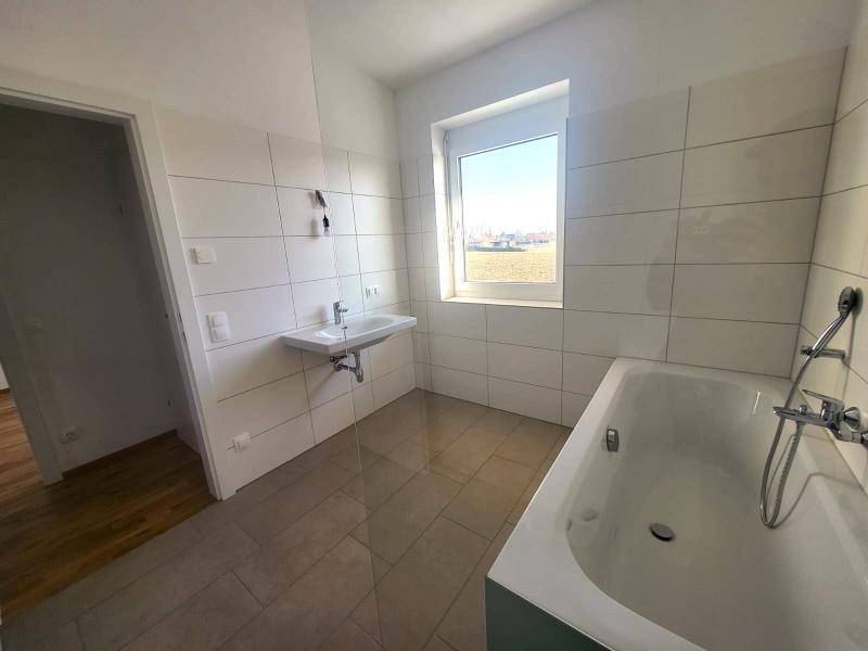 Modernes Badezimmer mit Badewanne, Waschbecken und Fenster für natürliches Tageslicht.