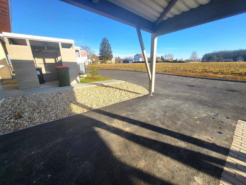Überdachter Stellplatz (Carport) mit angrenzendem Mülltonnenbereich und Feld im Hintergrund.
