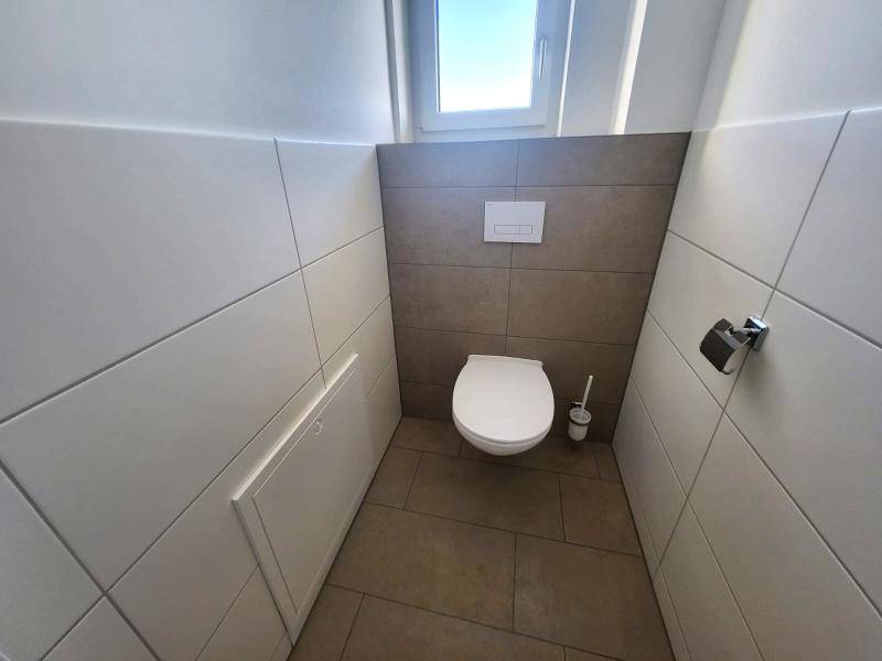 Separate Toilette mit Wand-WC und Fliesen in zwei Farbtönen, modern gestaltet.