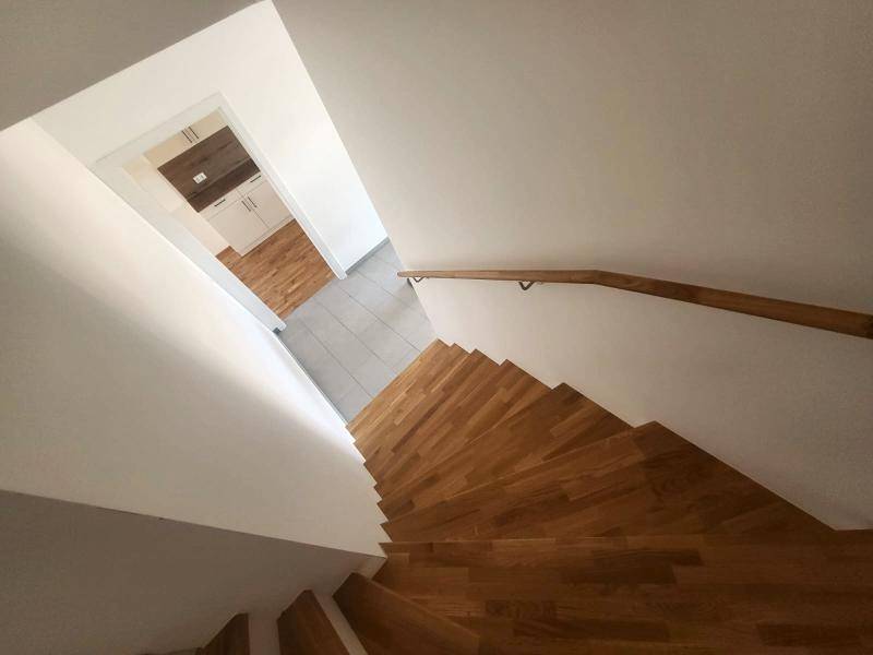 Treppenhaus mit Holzstufen und Handlauf, führt zu einem gefliesten Bereich im Erdgeschoss.