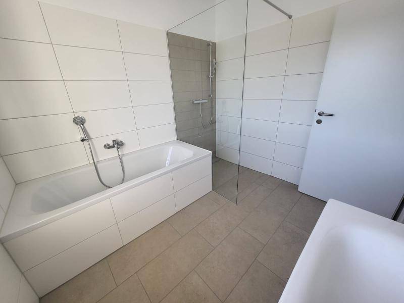 Badezimmer mit Badewanne, Duschbereich und Fliesenboden in neutralen Farben.