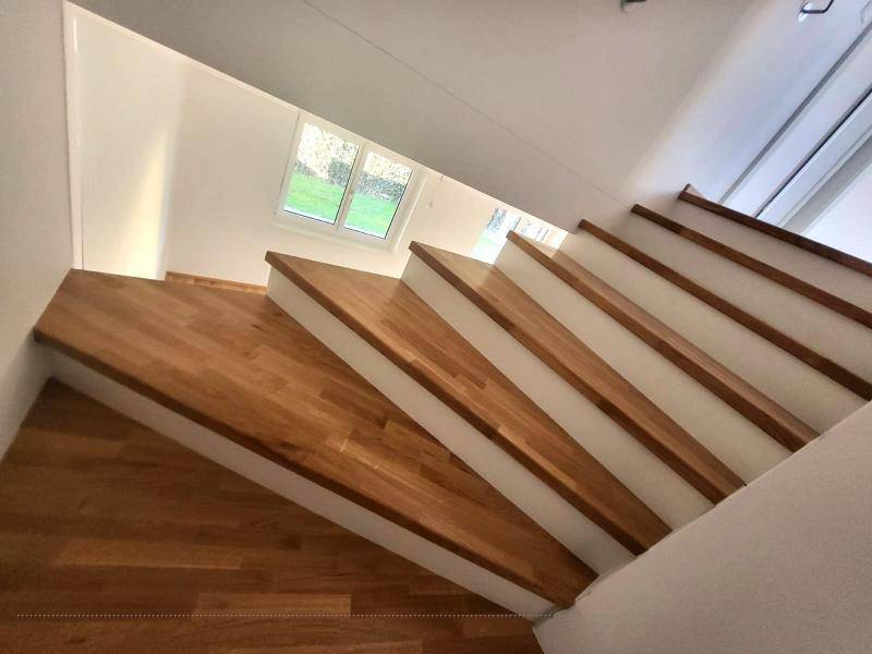 Holztreppe mit weißem Geländer und Fenster, das Tageslicht in den Flur hereinlässt.