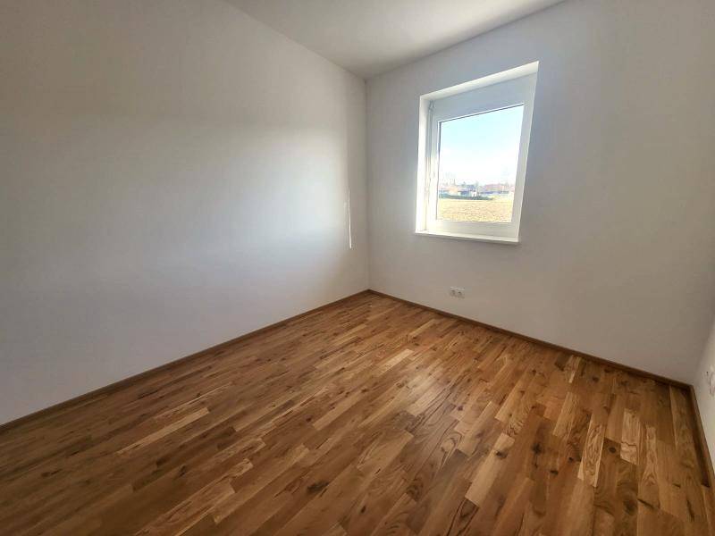 Ruhiges Schlafzimmer mit Holzboden und Fenster, das viel Tageslicht hereinlässt.