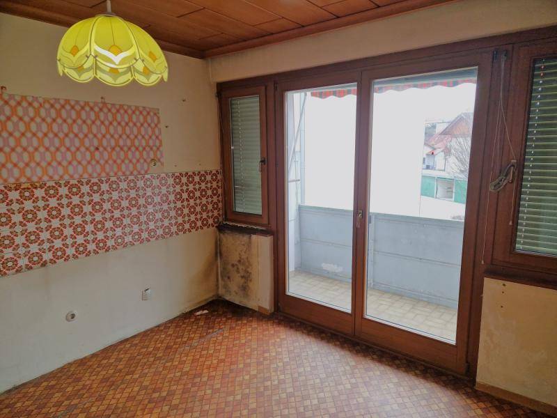 Zimmer mit Balkonzugang, gemustertem Fliesenboden und sichtbaren Feuchtigkeitsspuren an der Wand.