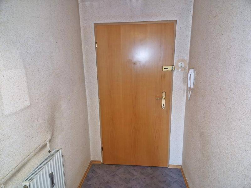 Eingangsbereich mit Holztür, strukturierten Tapeten und einem Heizkörper, typisch für ältere Gebäude.