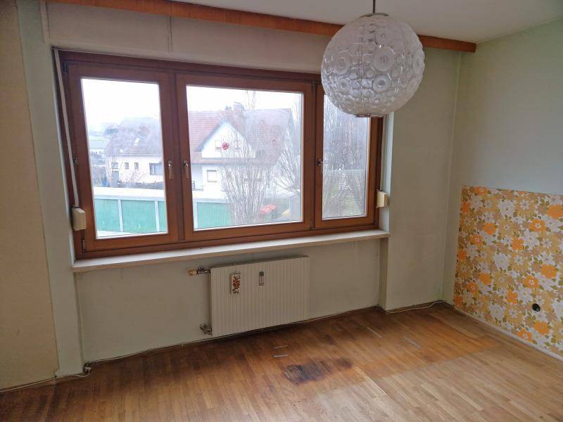 Helles Zimmer mit Holzboden, Heizkörper und einem Fenster mit Blick auf die Nachbarschaft.
